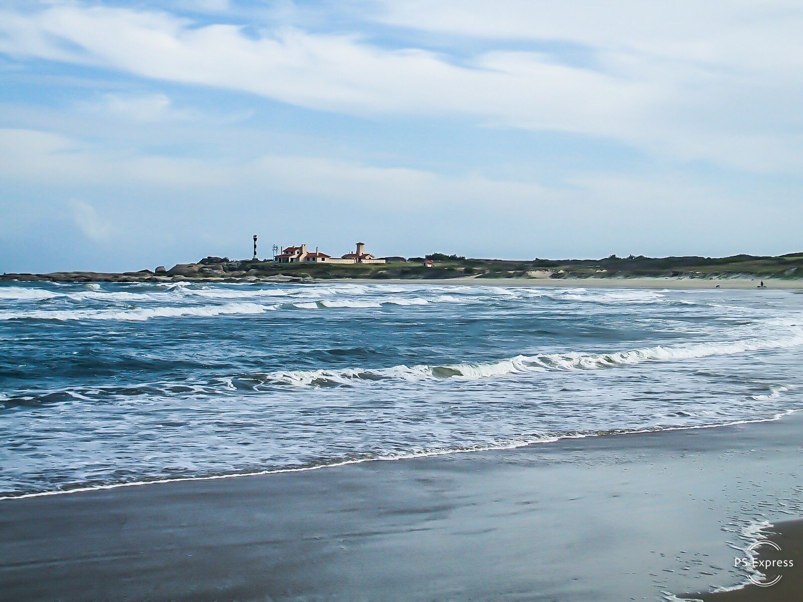 Una playa con olas rompiendo en la arena y un faro en la distancia.