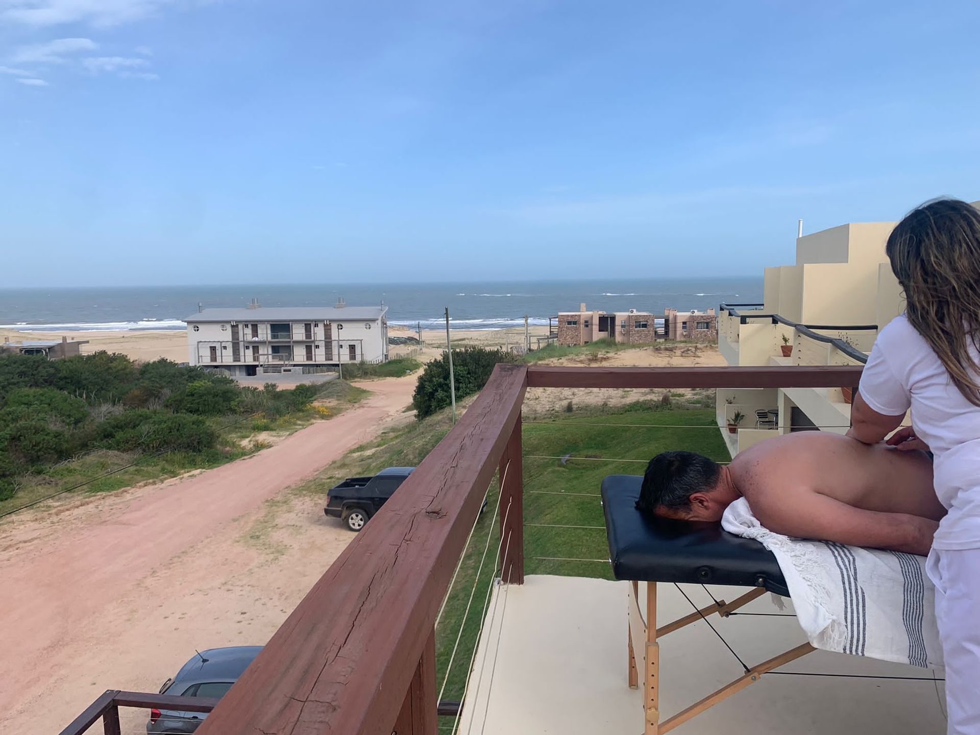 Una mujer le está dando un masaje a un hombre en un balcón con vista al océano.