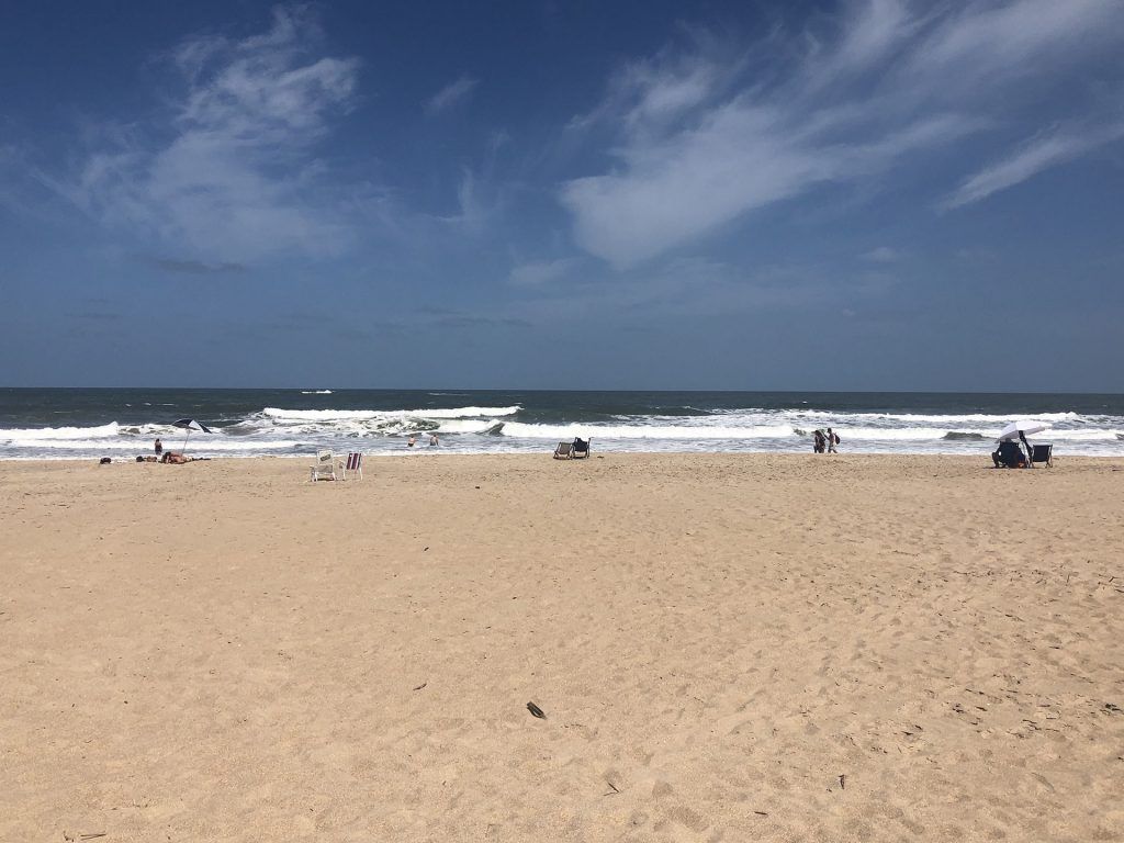 Una playa de arena con un cielo azul y nubes al fondo.