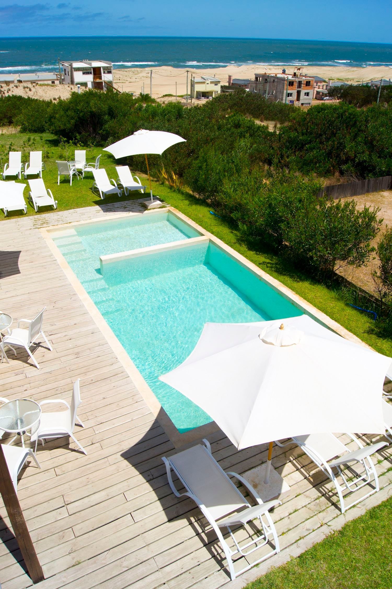 Una gran piscina rodeada de sillas y sombrillas con una playa al fondo.