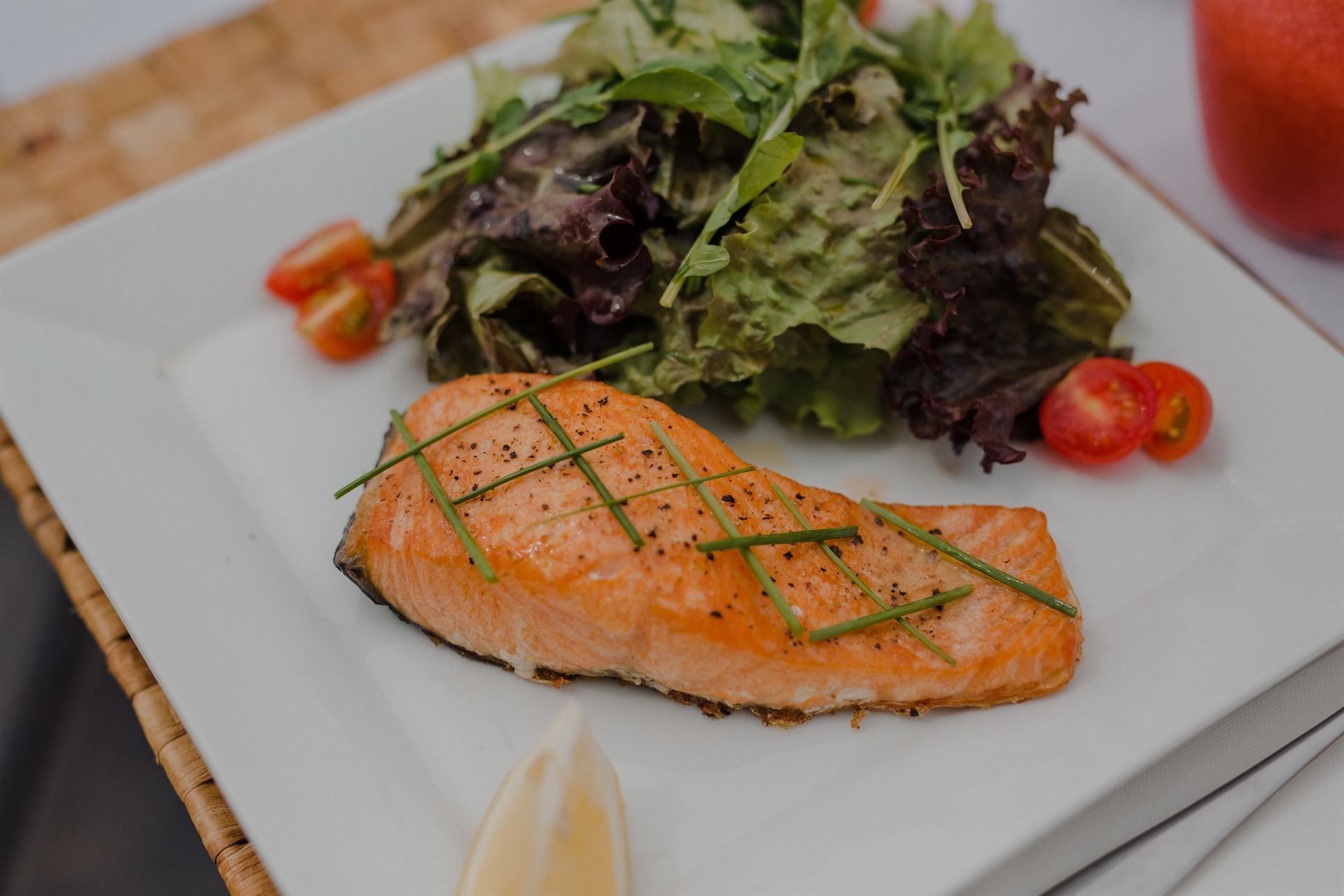 Un plato blanco cubierto con un trozo de salmón y una ensalada.
