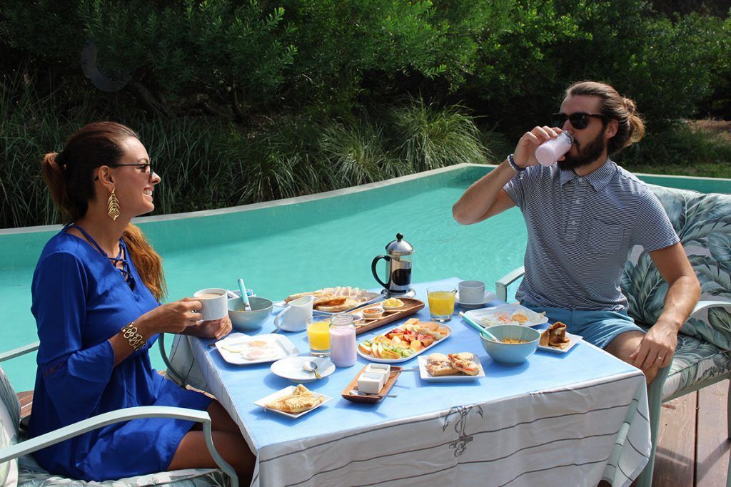 Un hombre y una mujer están sentados en una mesa con comida frente a una piscina.