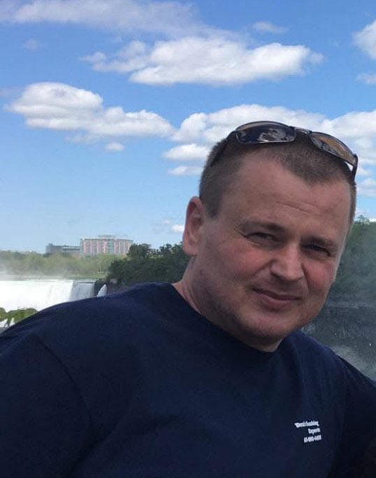 A man wearing sunglasses is standing in front of a waterfall.