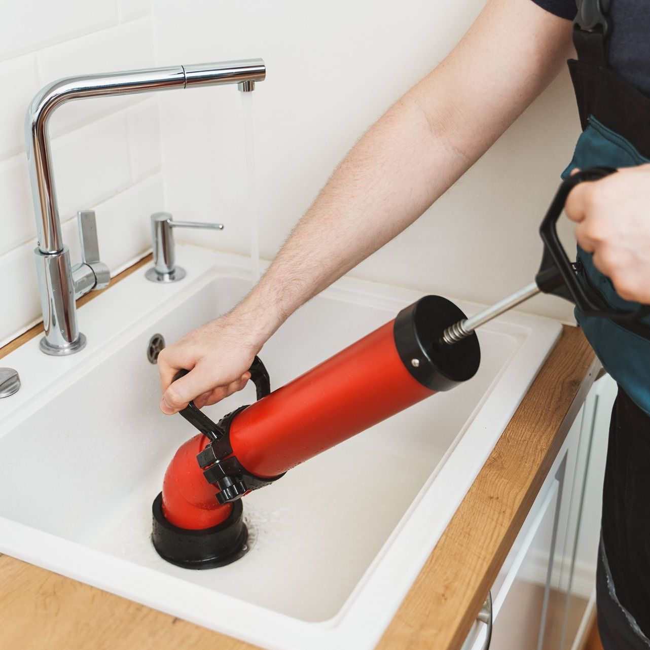 A person is using a red plunger to clean a sink