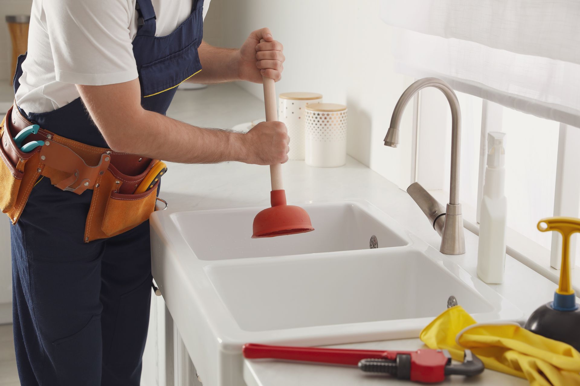 A plumber is using a plunger to unblock a kitchen sink.