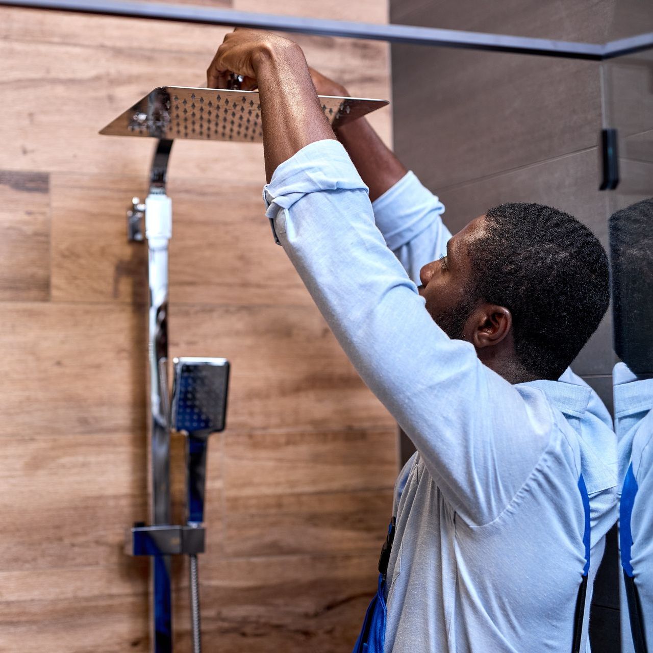 A man is fixing a shower head in a bathroom.