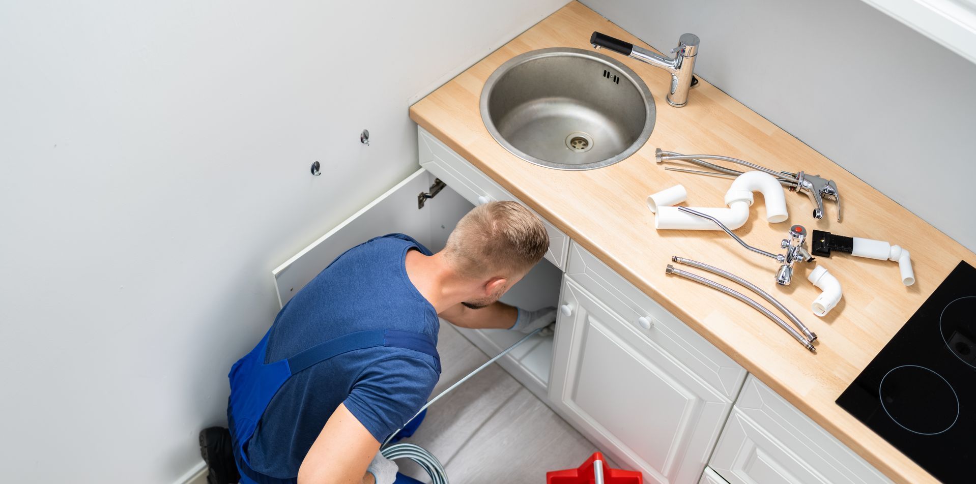 A plumber is fixing a sink in a kitchen.