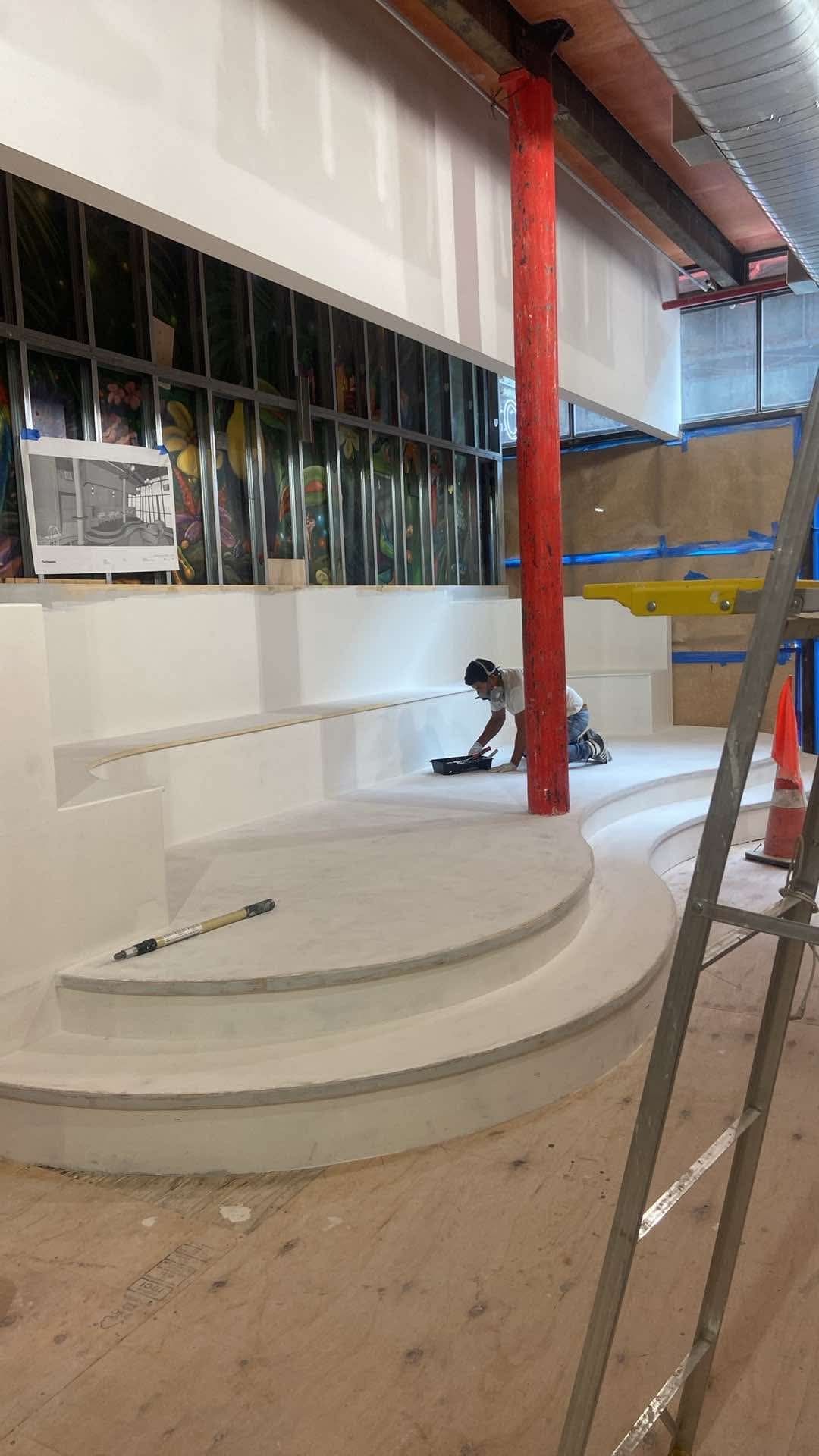 A man is kneeling on the floor in a room with a ladder.