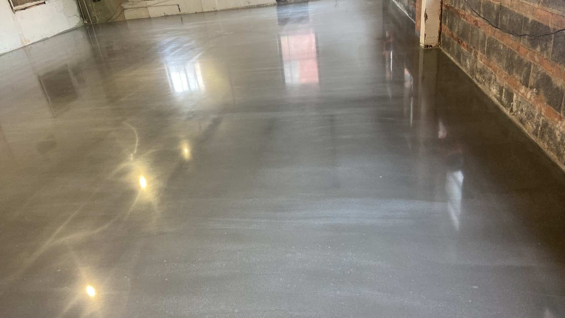 A shiny concrete floor in a room with a brick wall.