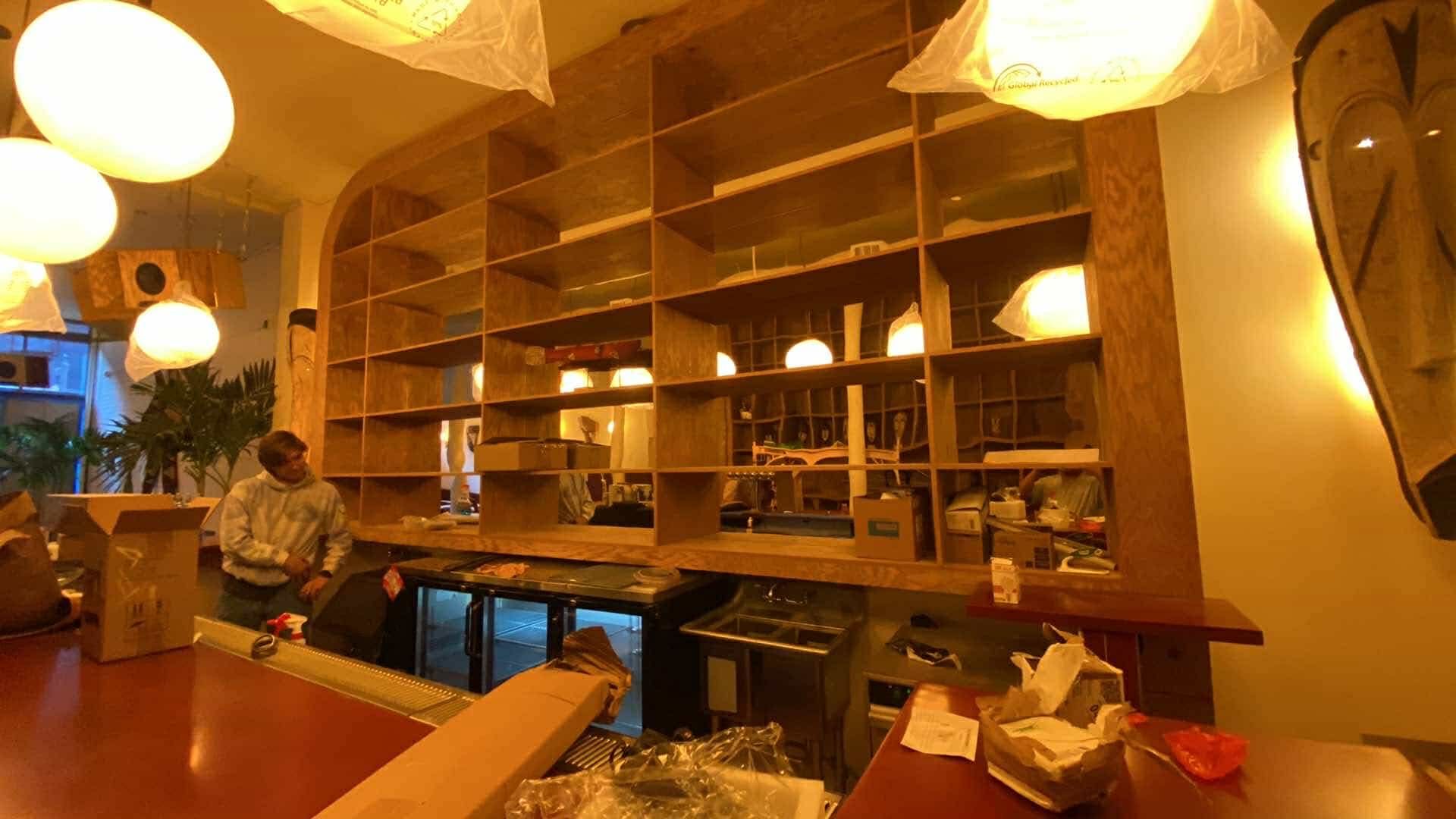 A man is standing behind a counter in a restaurant with empty shelves.