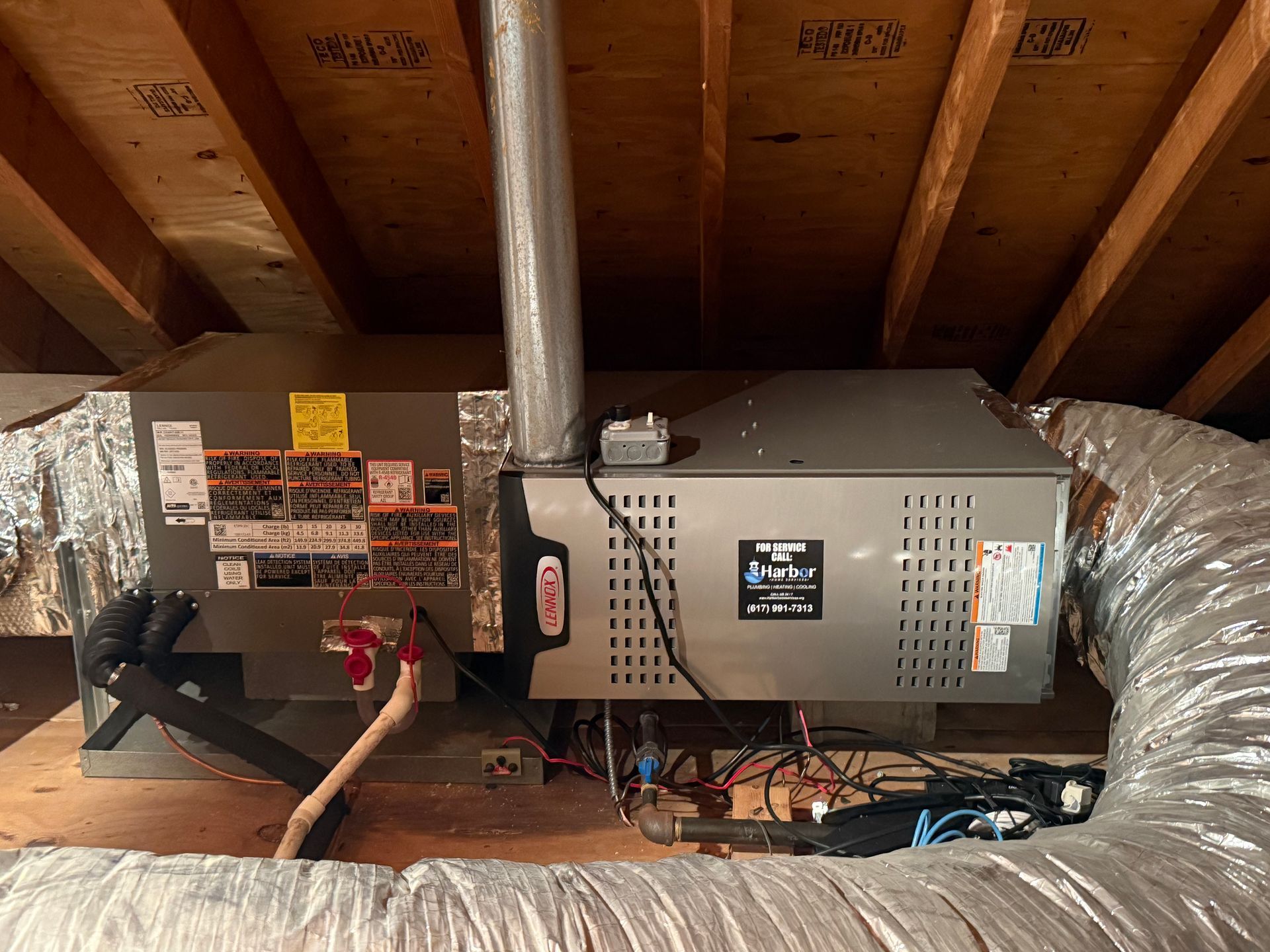 HVAC unit in an attic. Gray metal furnace with ductwork and pipes, wooden rafters in the background.