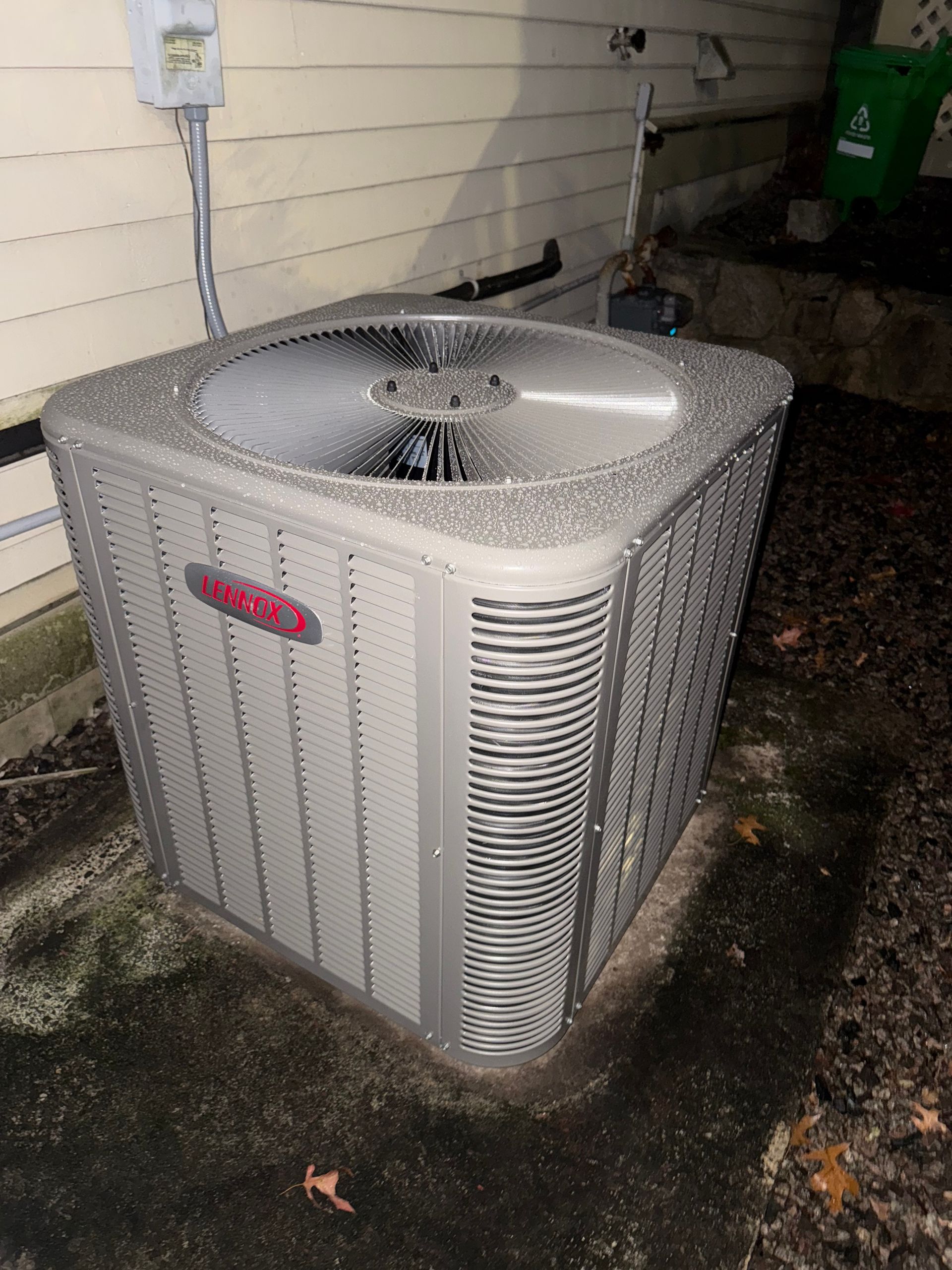 Outdoor air conditioning unit covered in ice, likely malfunctioning. Gray unit next to a building.