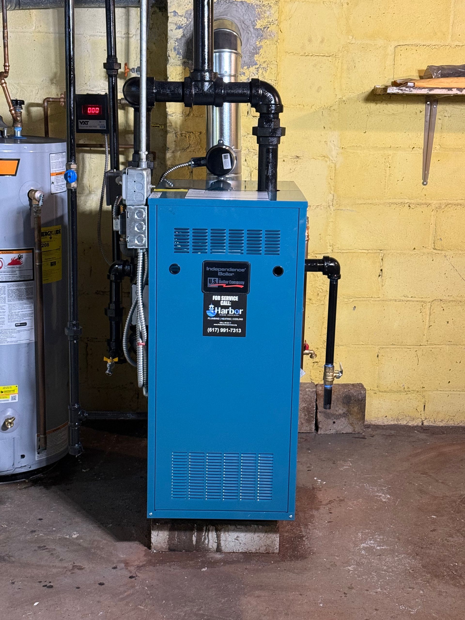 Blue boiler in a basement. Black pipes on top and right. Brick and concrete floor.