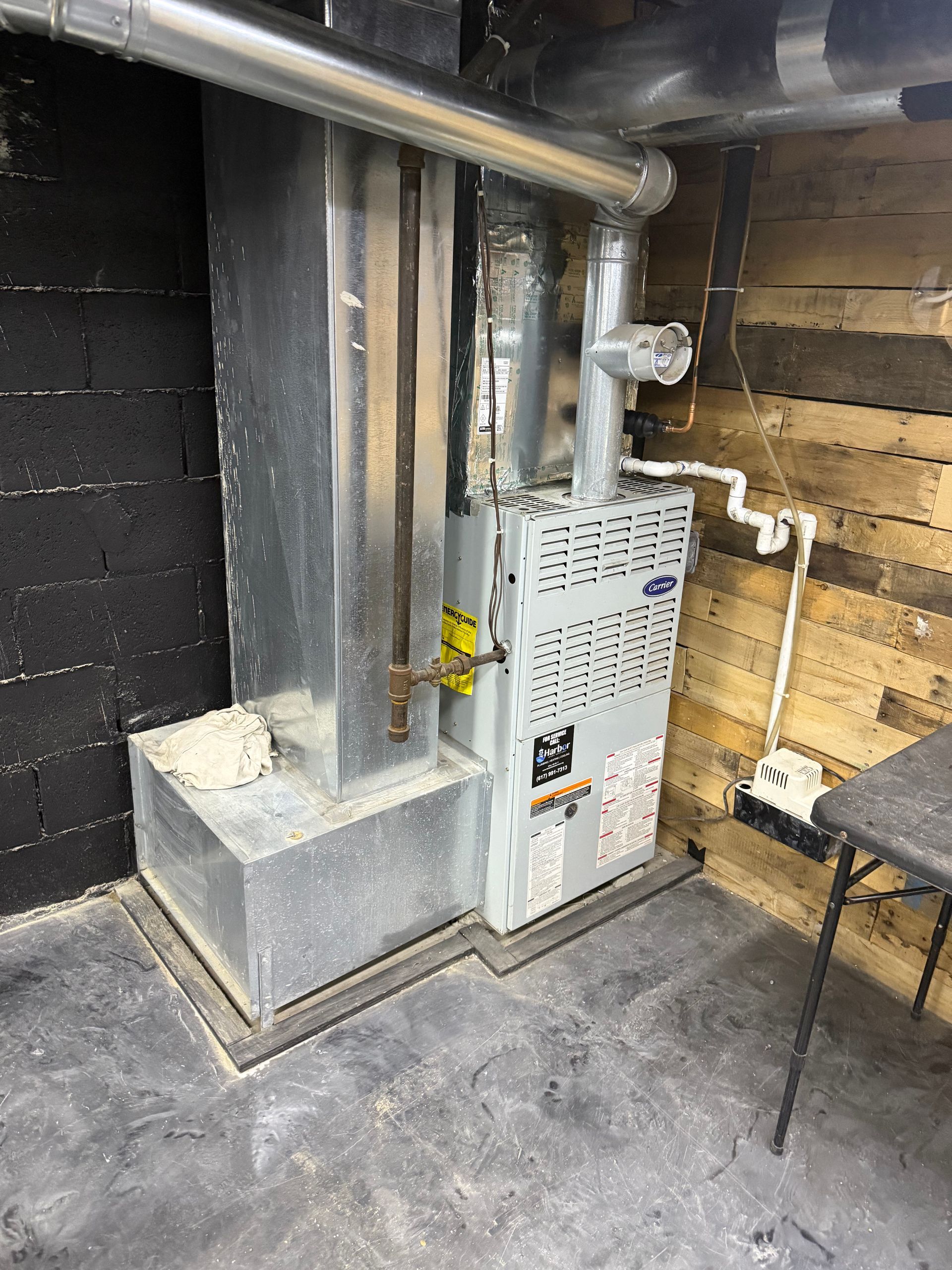 Furnace and ductwork in a basement. Silver metal against dark block and wood panel walls.
