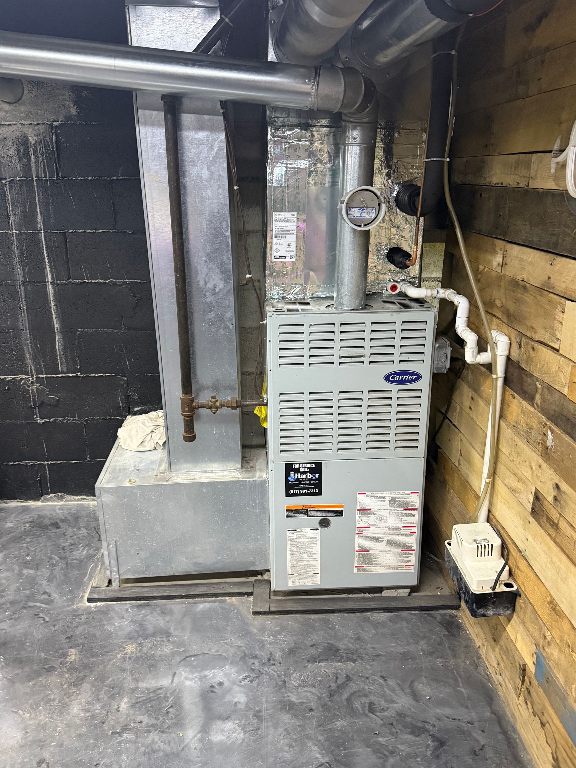 Furnace unit in a basement setting with ductwork and a gray metal casing.