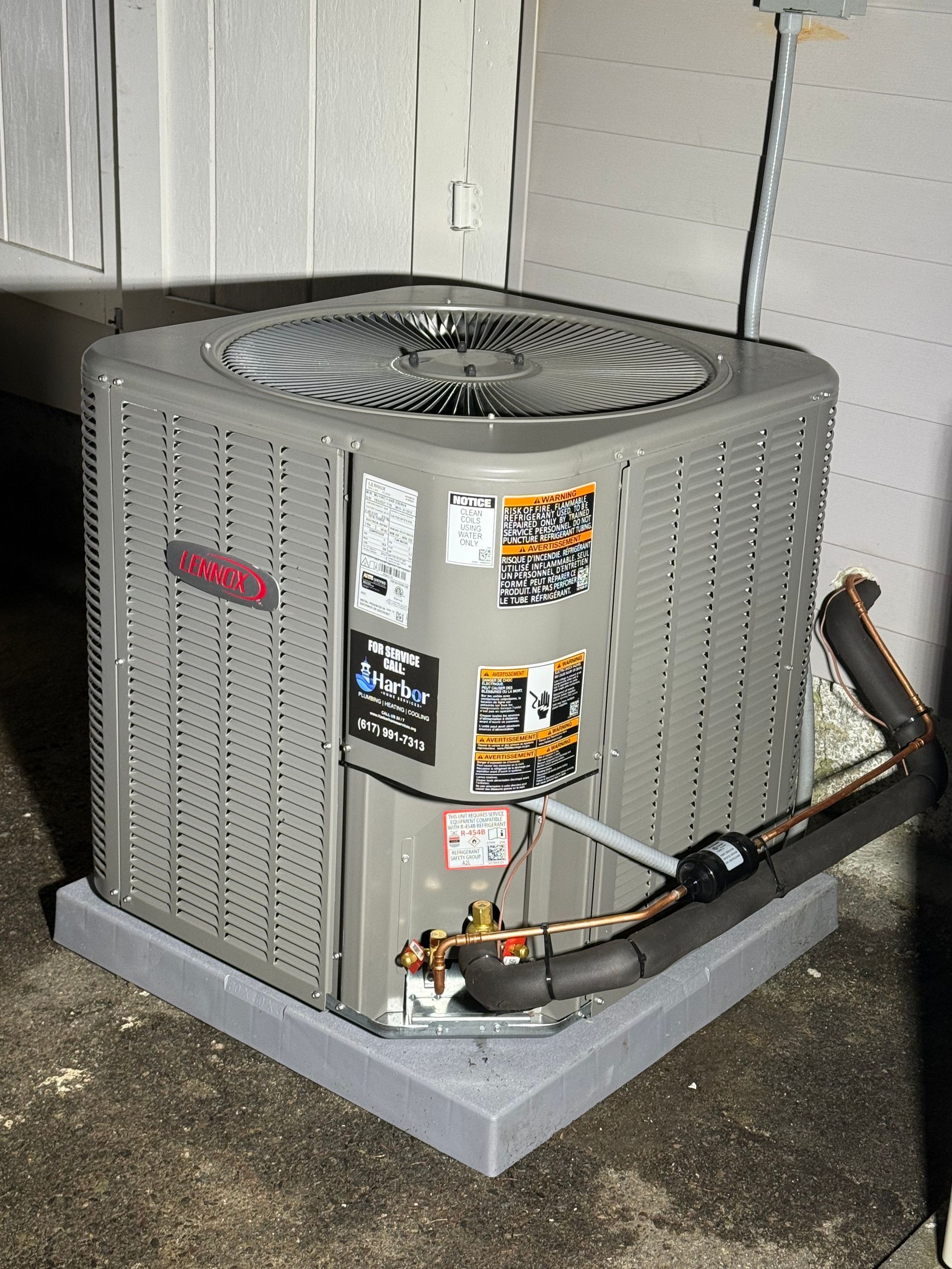 Gray Lennox air conditioning unit on a concrete pad next to a wall.