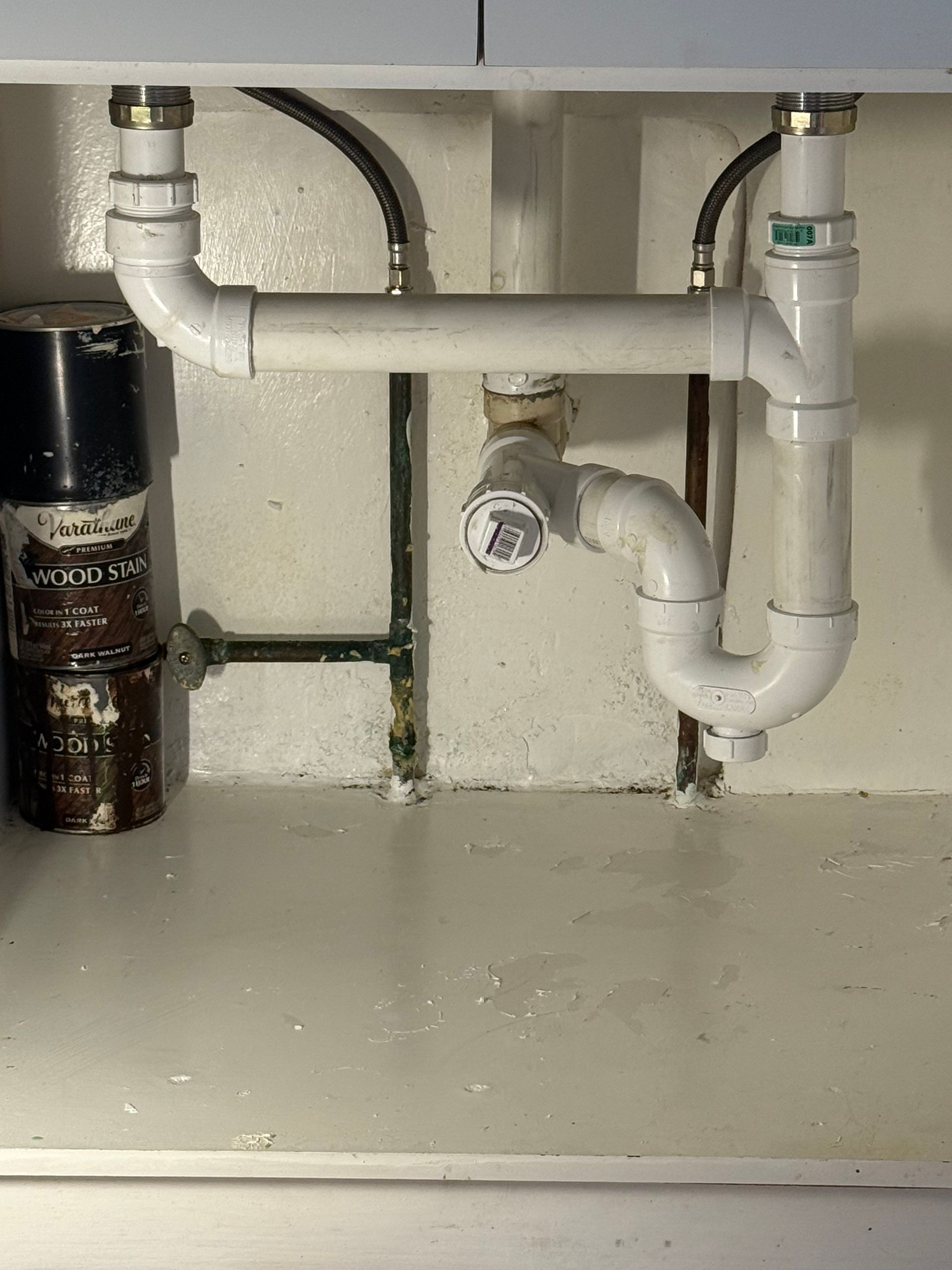 Under-sink plumbing: white pipes, a black garbage disposal, and a white cabinet.