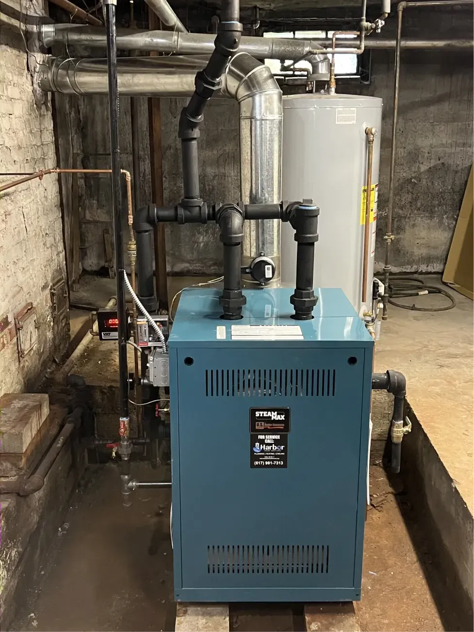 Blue boiler in a basement, with black pipes and a silver water heater behind it.