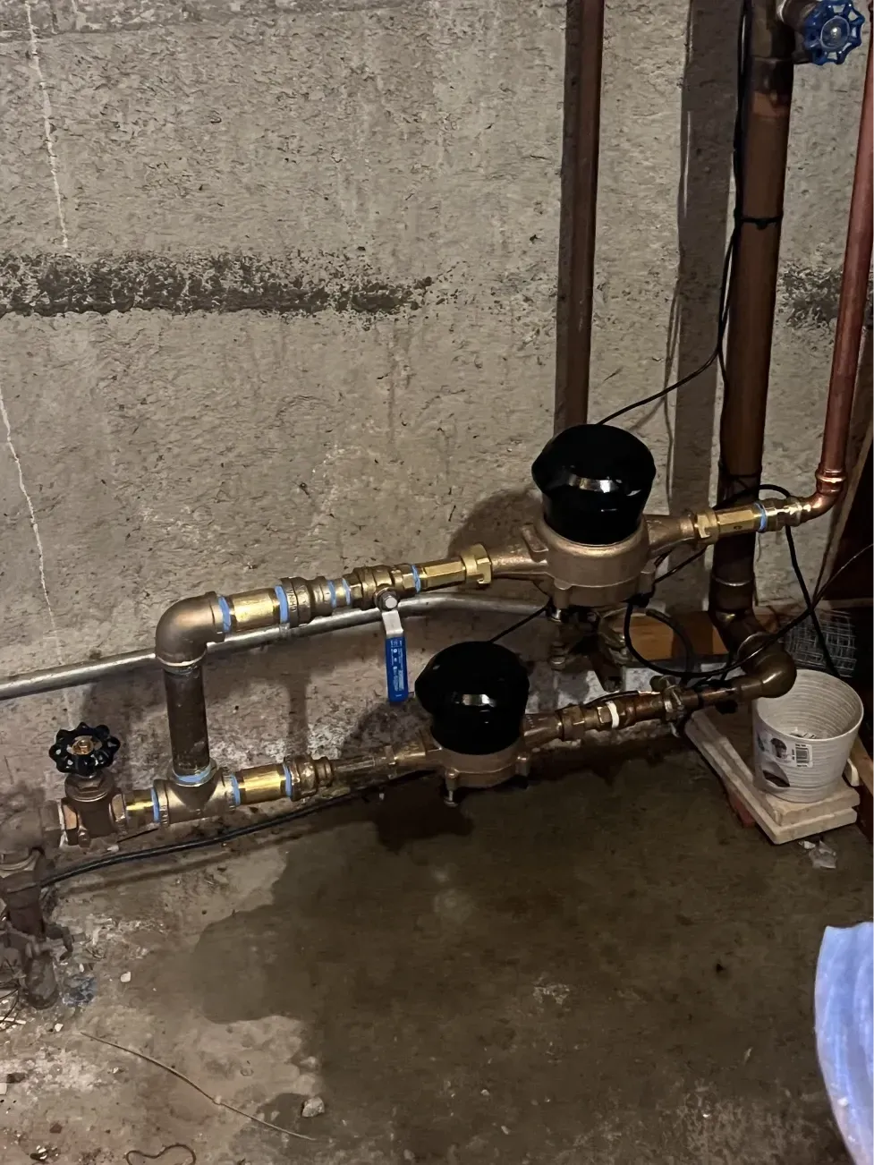 Plumbing pipes with two black-topped backflow preventers against a concrete wall.