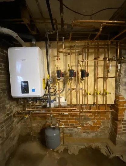 White tankless water heater and copper pipes mounted on a wooden panel in a brick basement.