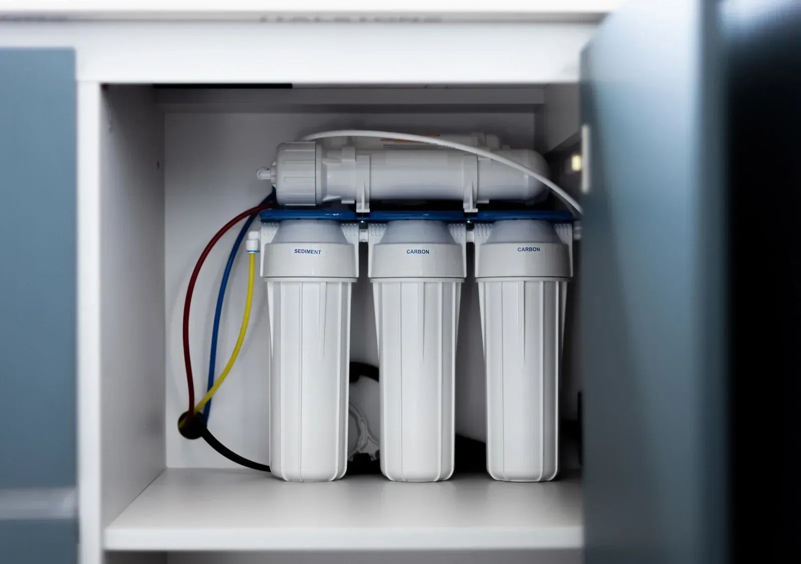 Under-sink water filter system with three white canisters and colored tubing
