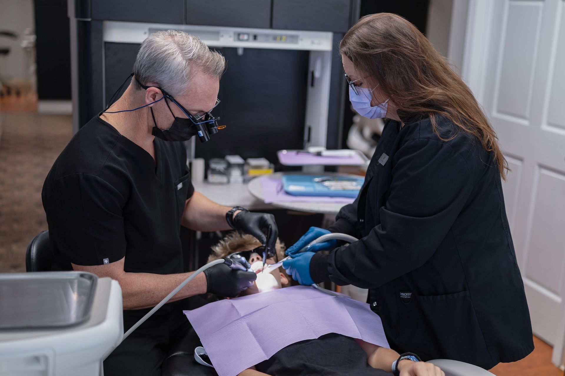 Dentist and dental hygienist cleaning young patient's teeth