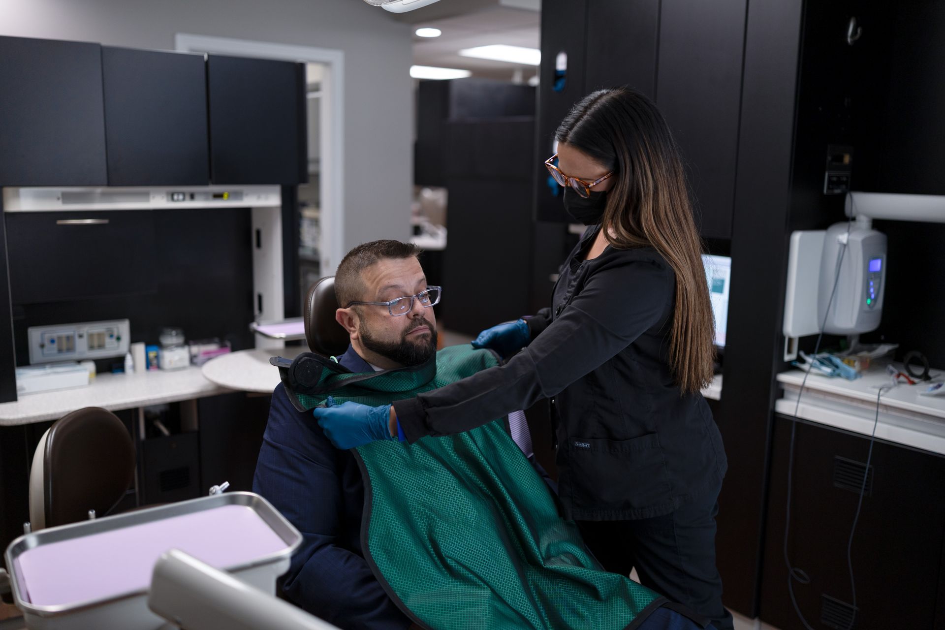 Dental assistant putting bib on patient in a dental chair
