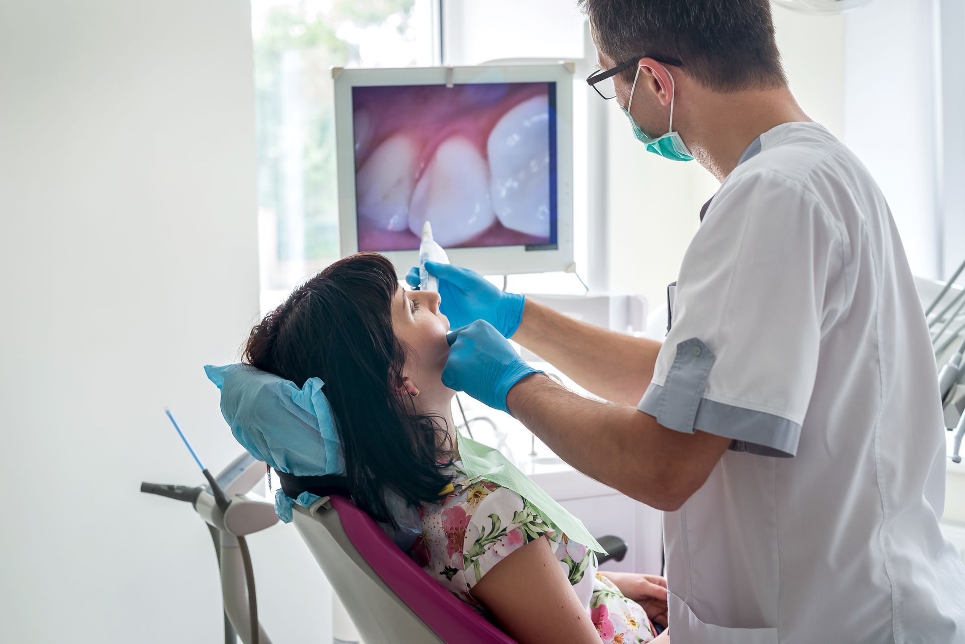 A woman is sitting in a dental chair while a dentist examines her teeth.