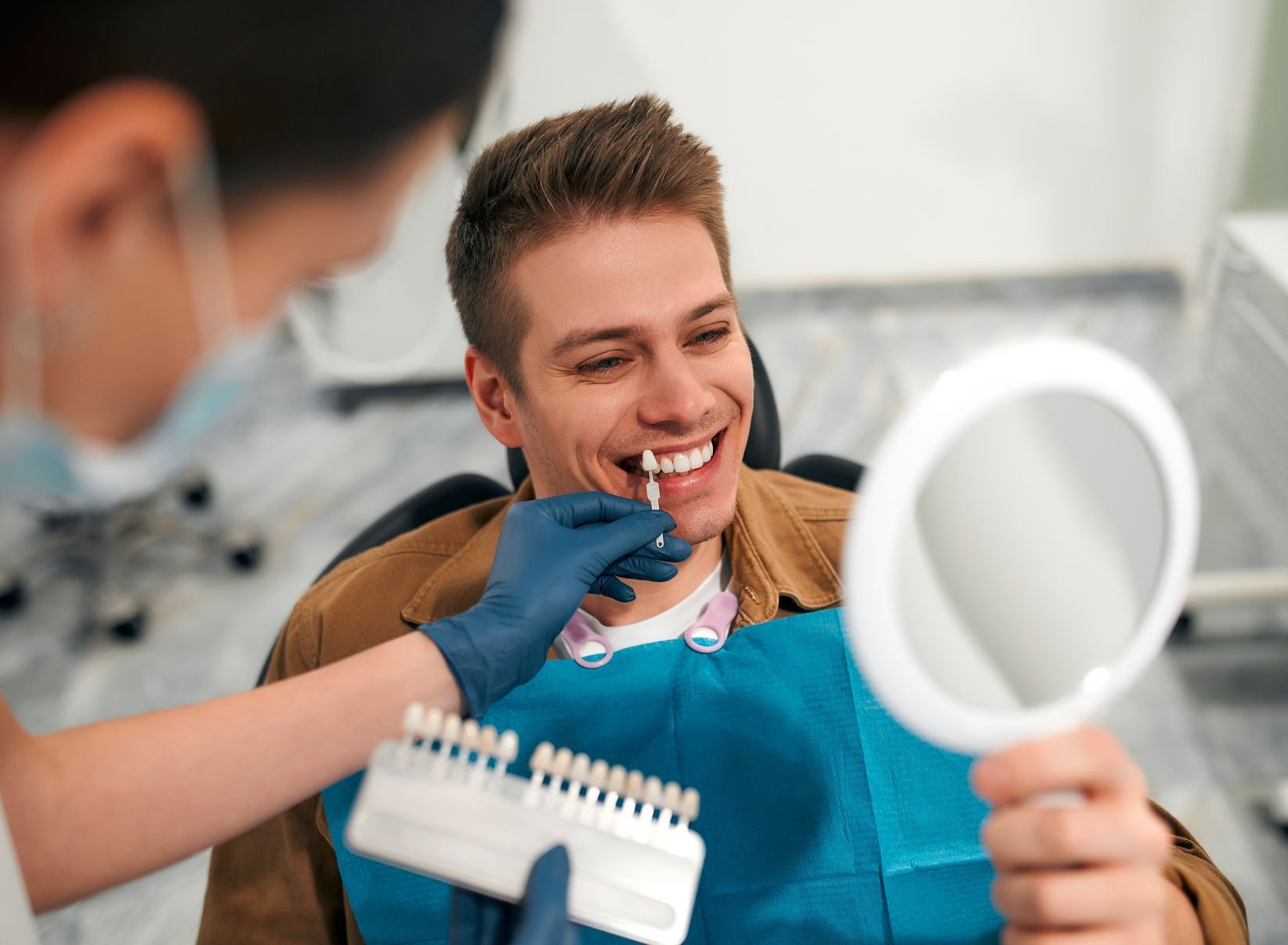 A man is sitting in a dental chair looking at his teeth in a mirror.