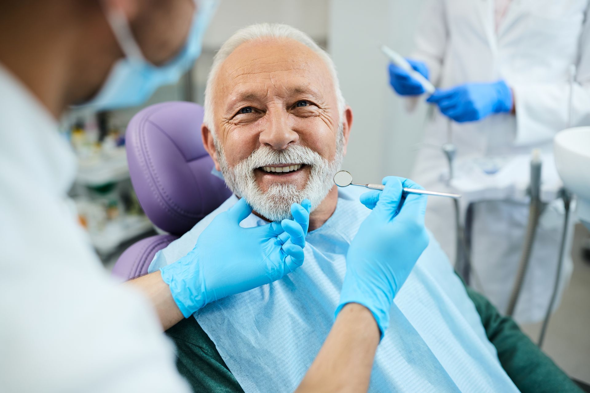 An elderly man is sitting in a dental chair while a dentist examines his teeth.