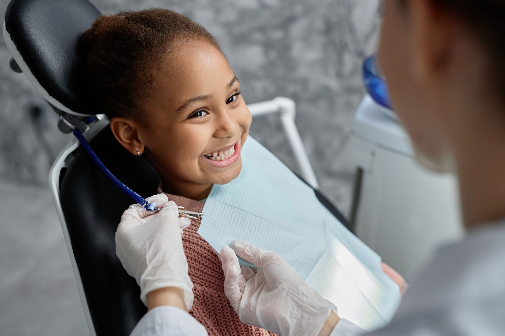 A little girl is sitting in a dental chair while a dentist examines her teeth.