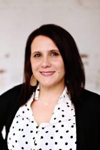 A woman wearing a polka dot shirt and a black jacket is smiling for the camera.