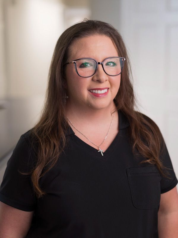 Dental hygienist wearing black outfit and glasses smiling at camera