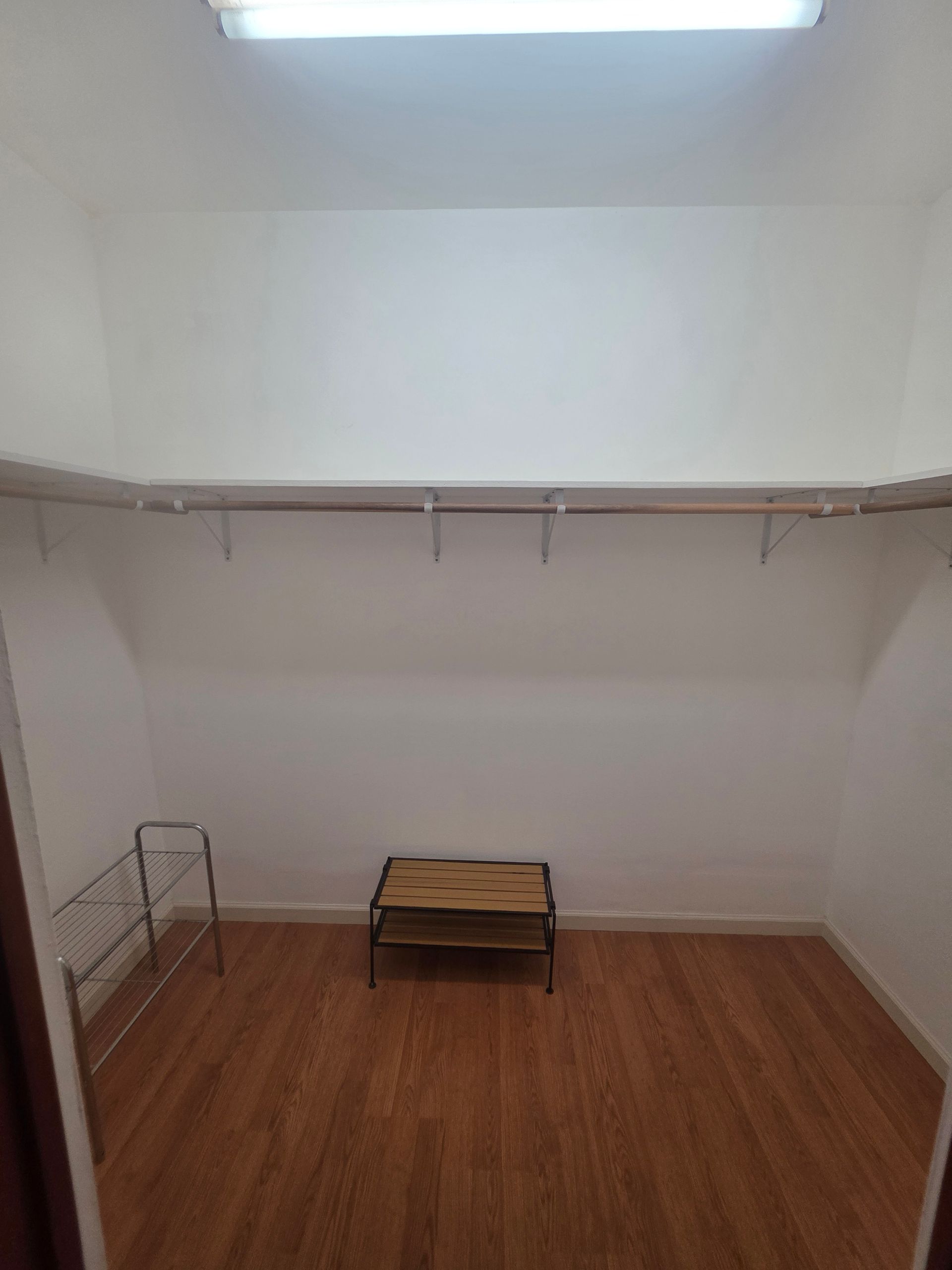Empty walk-in closet with wooden floor, shelving, and a small bench.