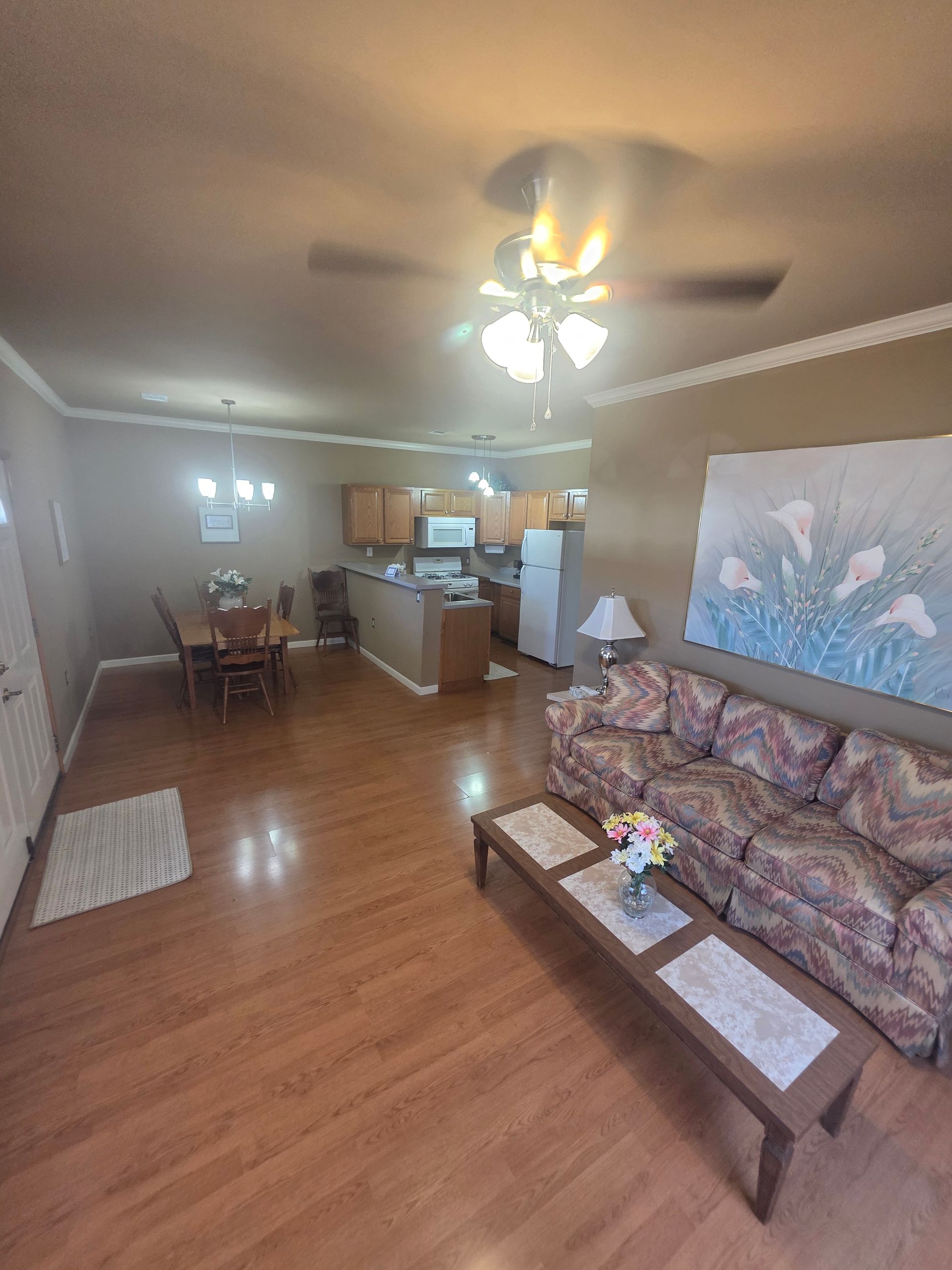 Living room with brown floors, kitchen visible. Brown couch, coffee table, dining table and open kitchen.