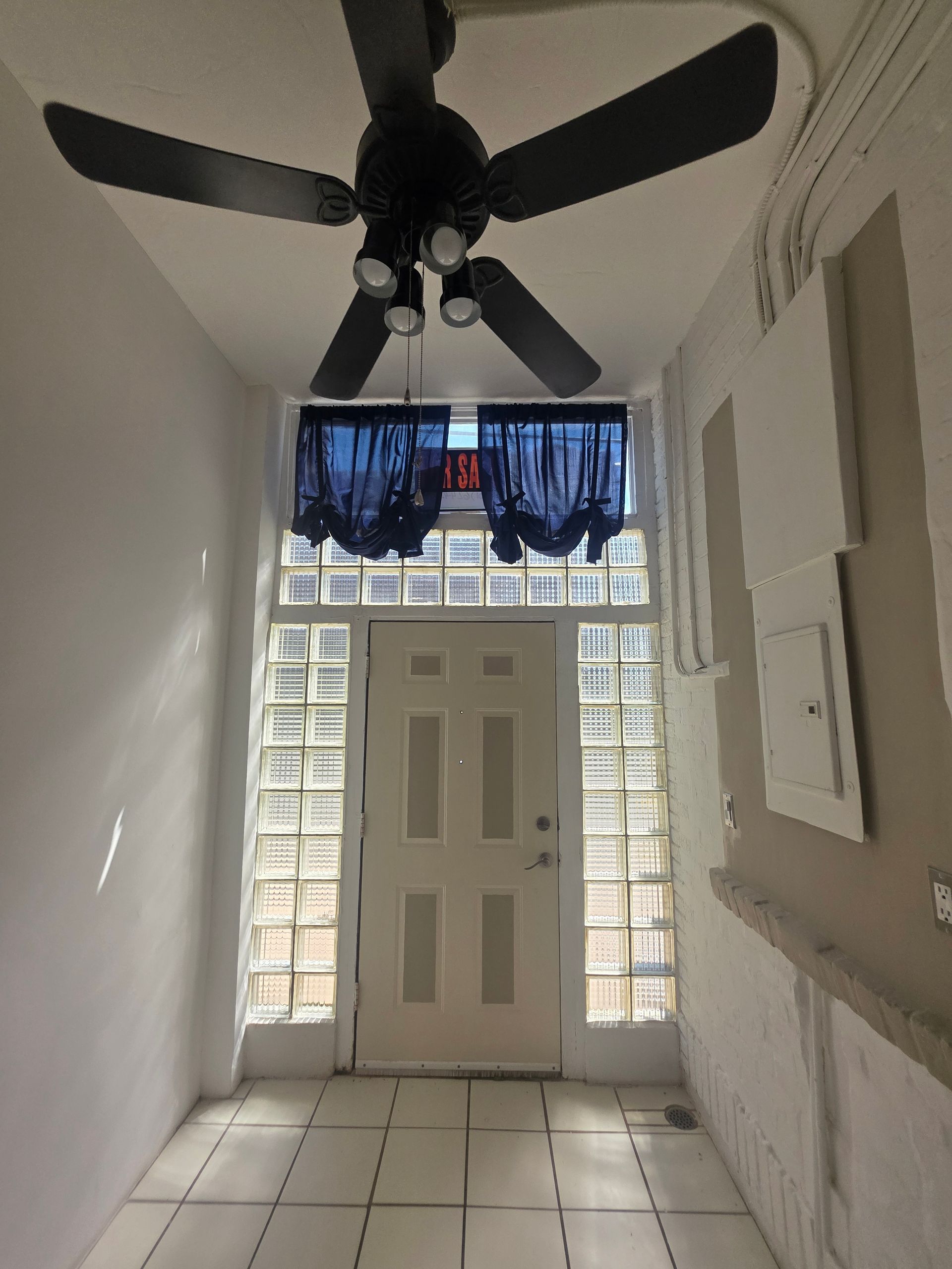 Narrow hallway with front door, glass block windows, ceiling fan, and tiled floor.