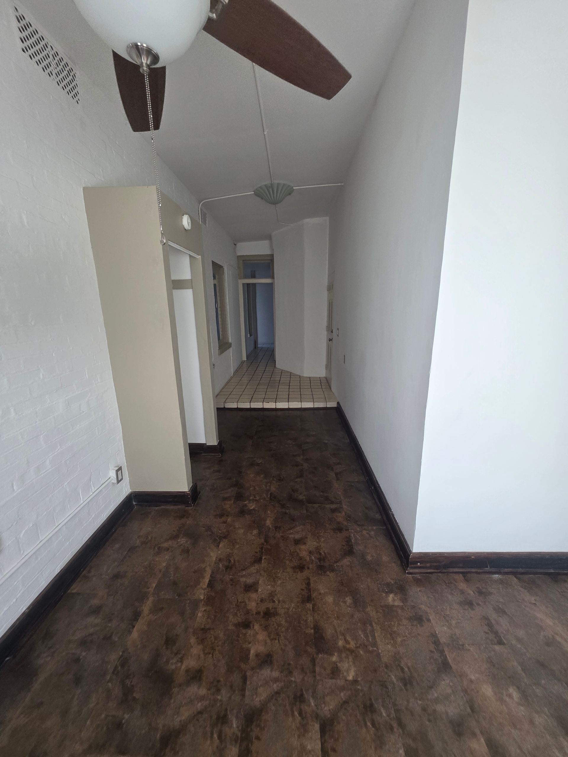 Narrow room with dark wood floor, white walls, and a ceiling fan.