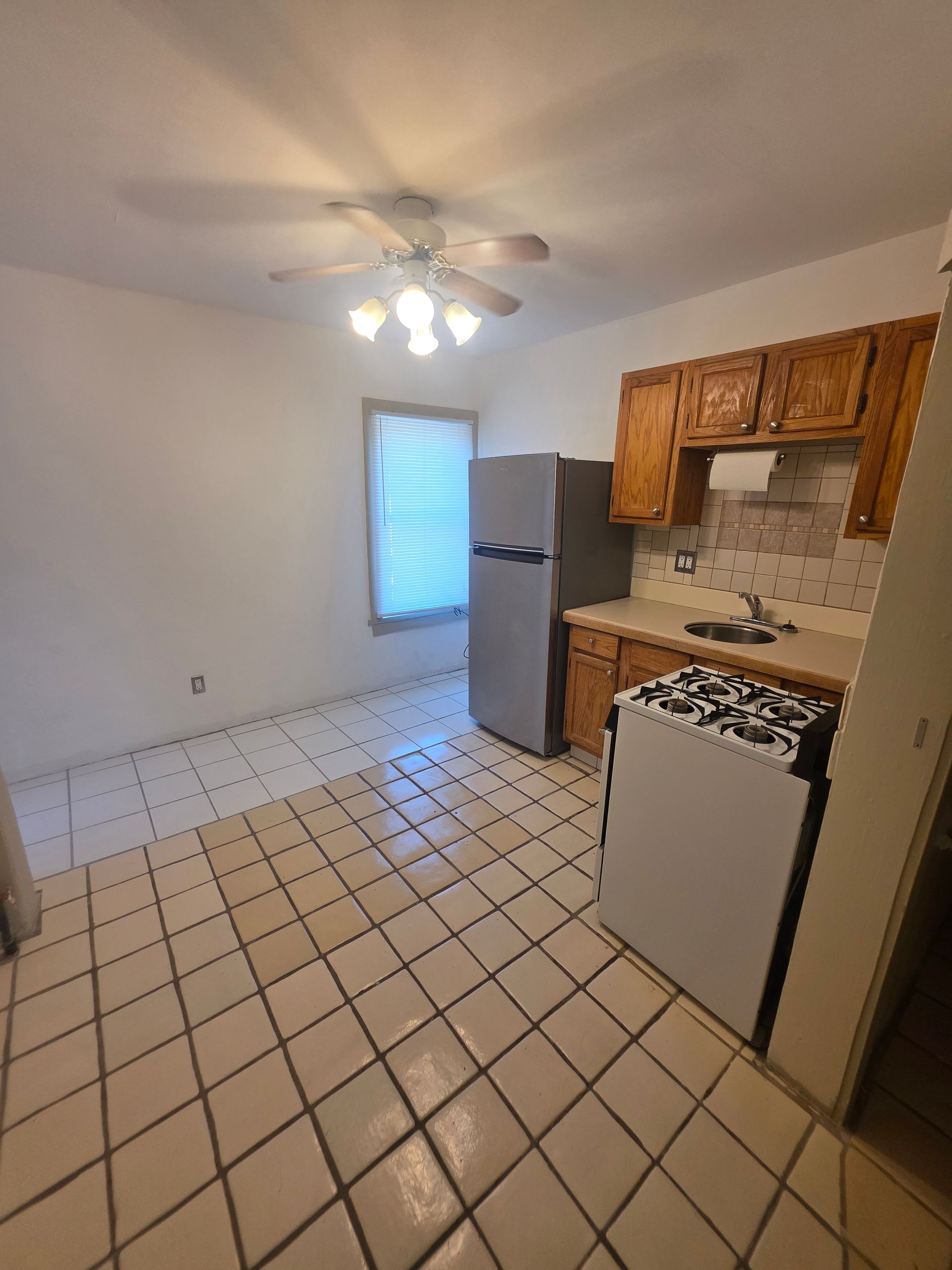 Kitchen with tile floor, cabinets, appliances, and a window.