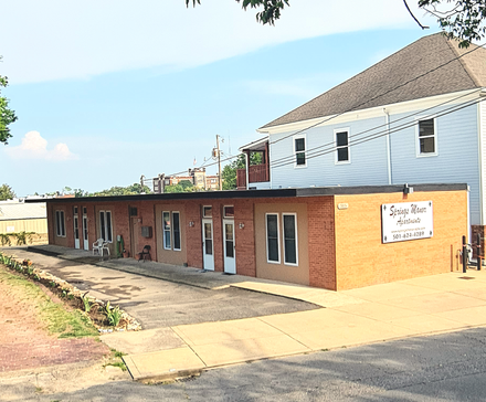 Brick building with multiple entrances next to a two-story house, sunny day.