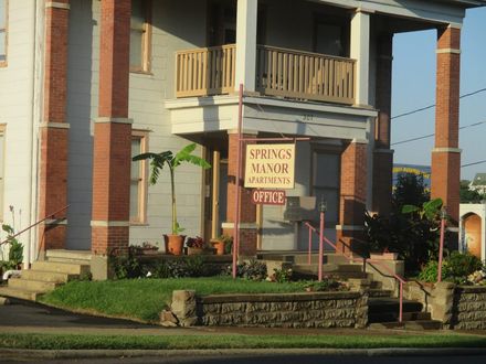 Springs Manor Apartments building with brick columns, sign, and grassy yard.