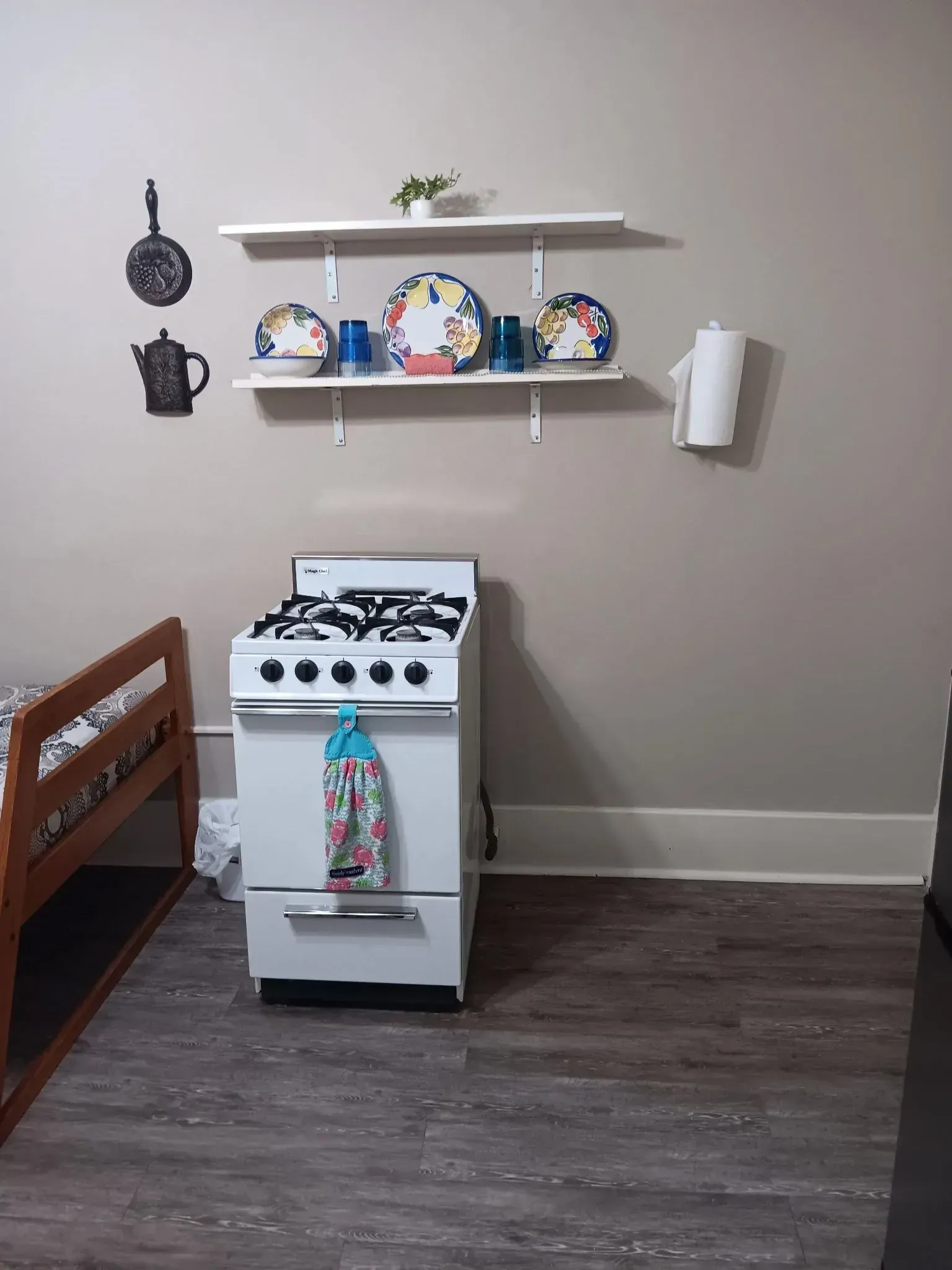 A kitchen with a stove , shelves , and a bunk bed.