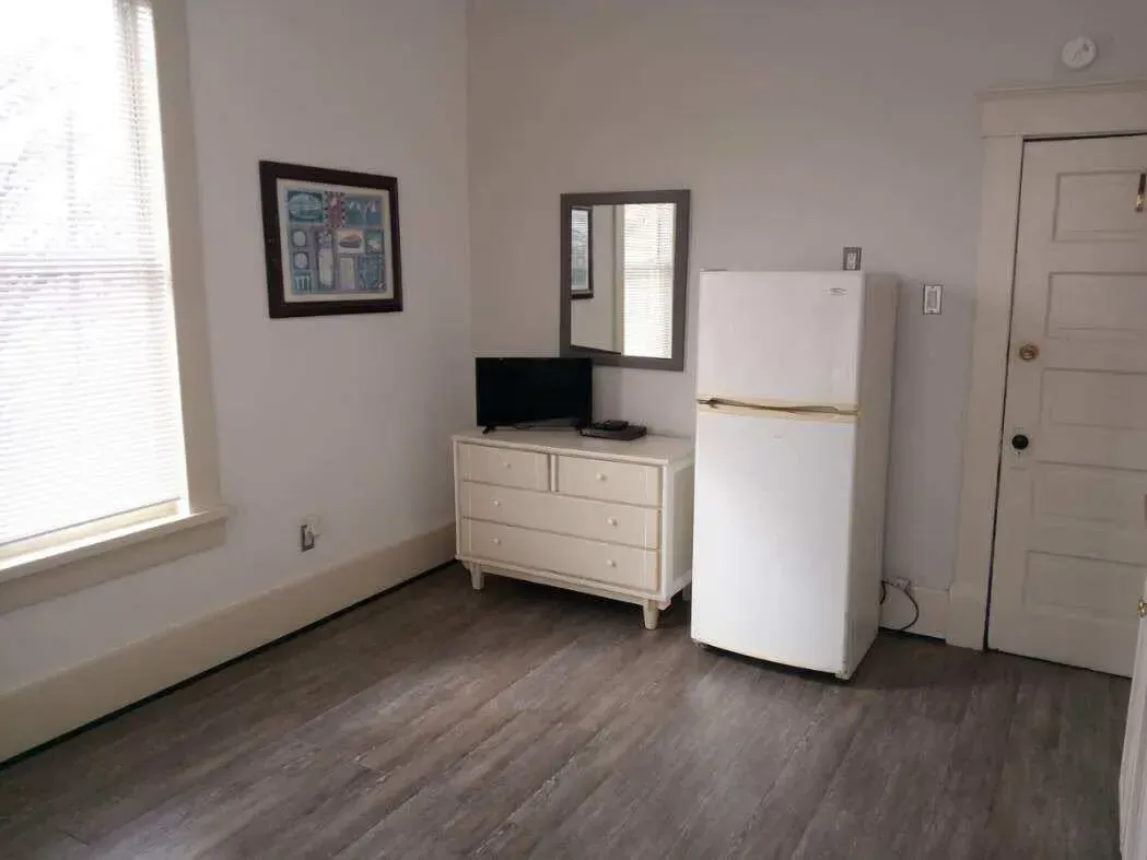 A room with a refrigerator , dresser , mirror and television.