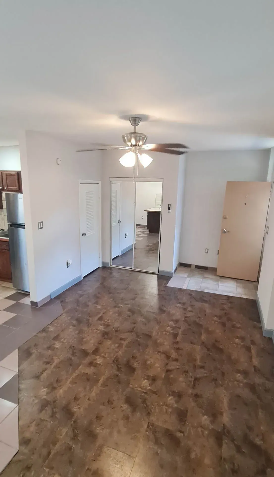 A living room with a ceiling fan and a door leading to a kitchen.