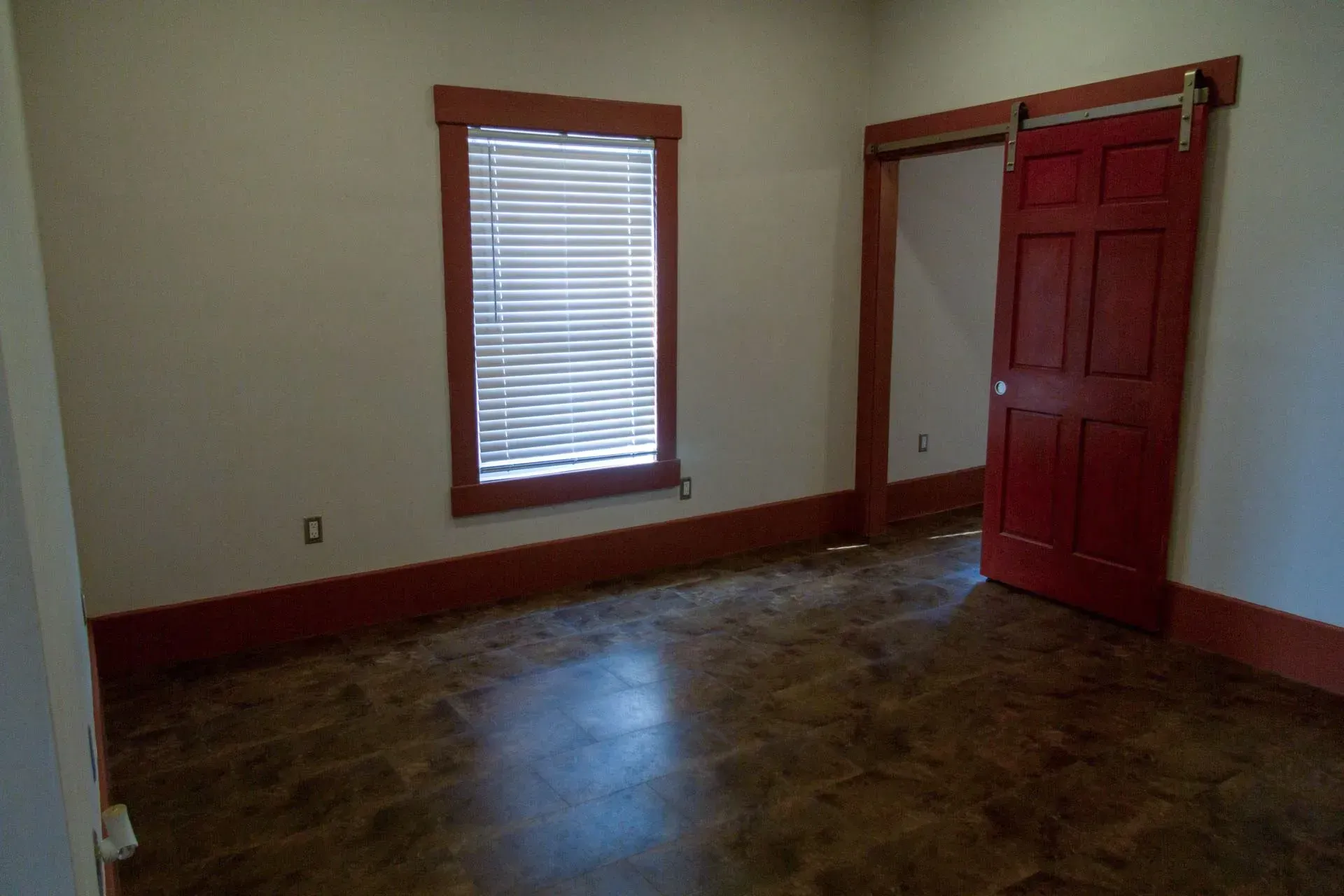 An empty room with a red door and two windows.
