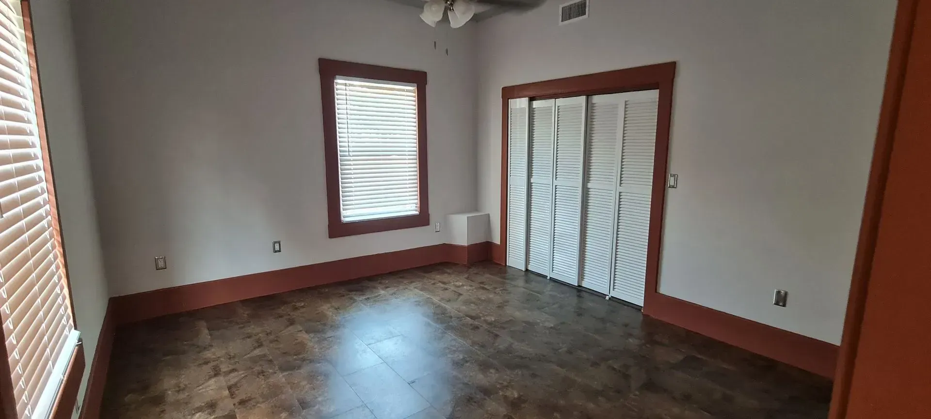 Empty room with dark wood floors and white walls, framed in orange. Includes closed blinds and a closet.