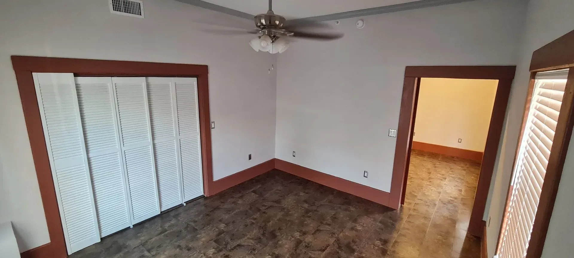 Interior view of a room with white walls, a ceiling fan, and brown trim. There is a closet and a doorway.