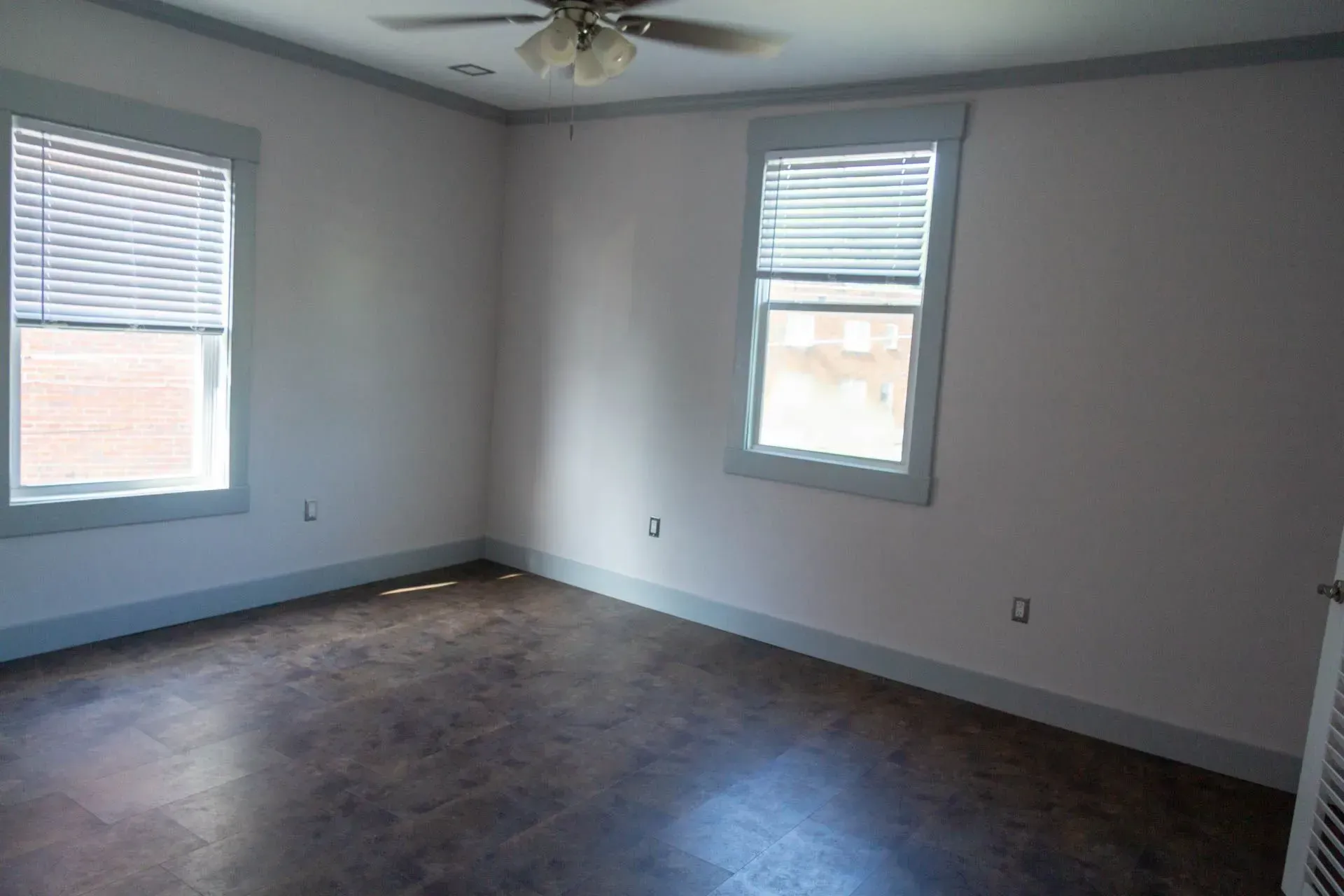 An empty room with a ceiling fan and two windows.