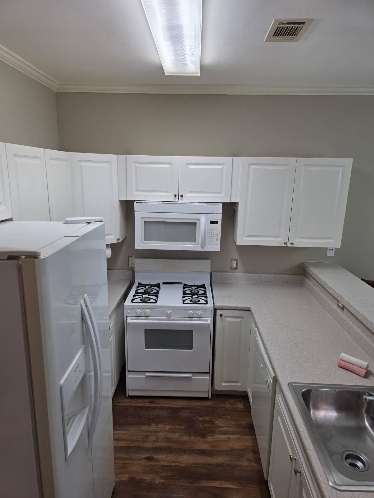 White kitchen: cabinets, appliances; oven, microwave. Refrigerator on left. Wood floor.