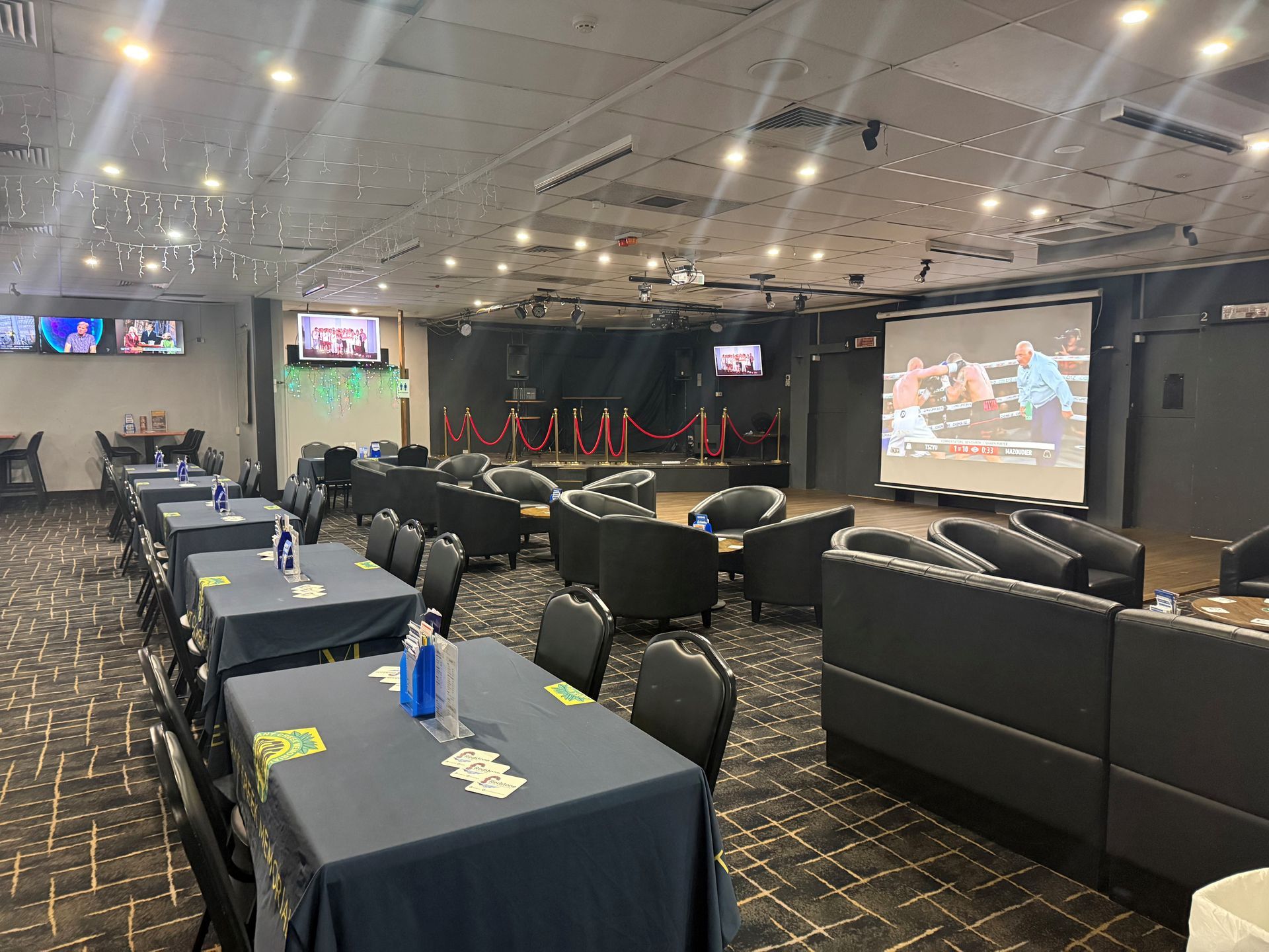Conference room with rows of black chairs and tables facing a large stage and projection screens  — Tennant Creek Memorial Club & Steak House in Tennant Creek, NT