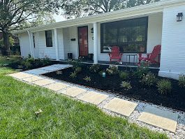White house with red door and chairs, square stepping stones, and dark mulch landscaping.